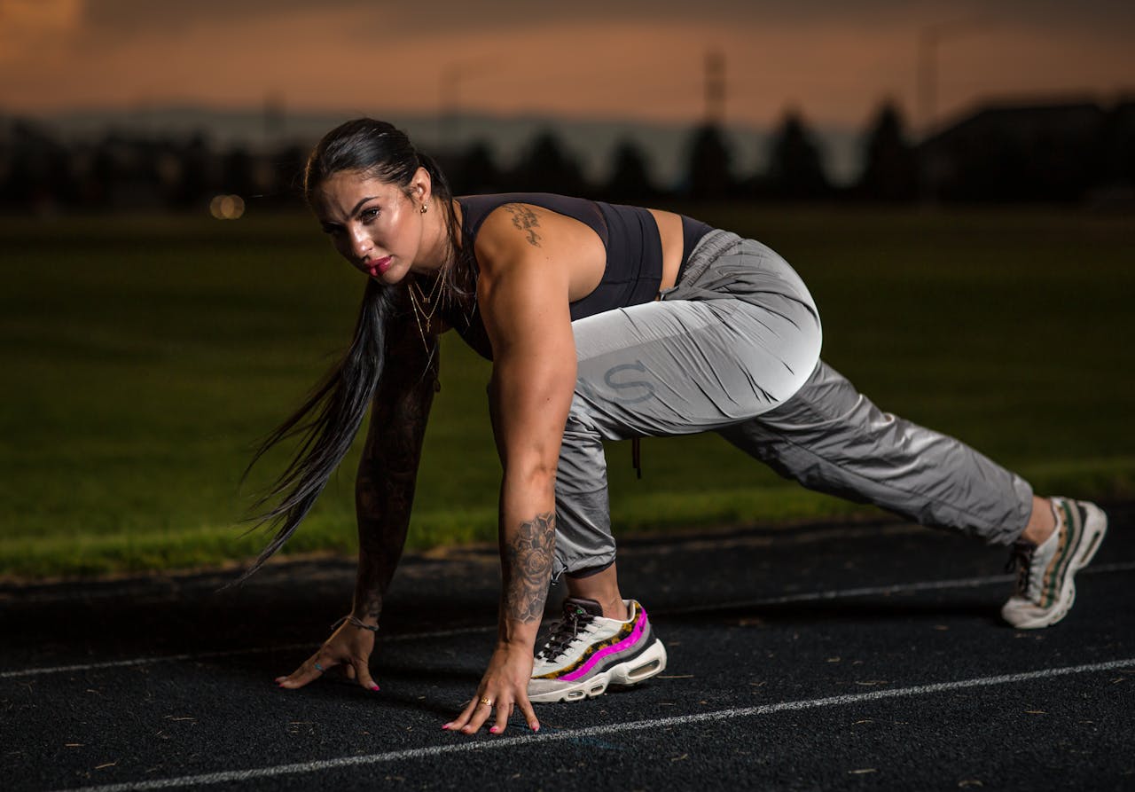 Female athlete in starting position on track at dusk, showcasing determination.